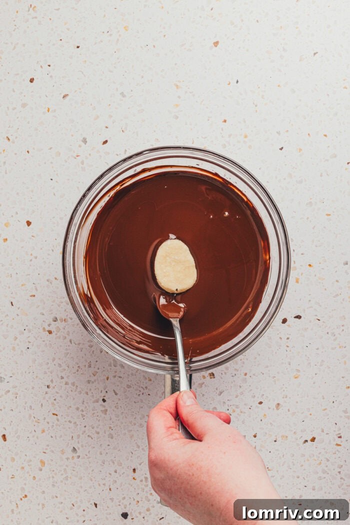 The egg-shaped filling being dipped into a bowl filled with melted chocolate.