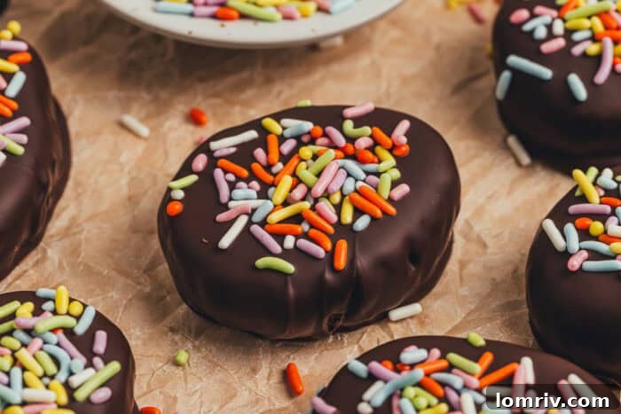 A few homemade chocolate Easter eggs scattered on parchment paper with a small plate filled with sprinkles.