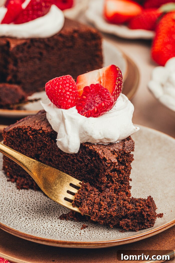 A close-up view of a chocolate ricotta cake slice, topped with creamy whipped cream and juicy berries, highlighting its inviting texture and presentation.