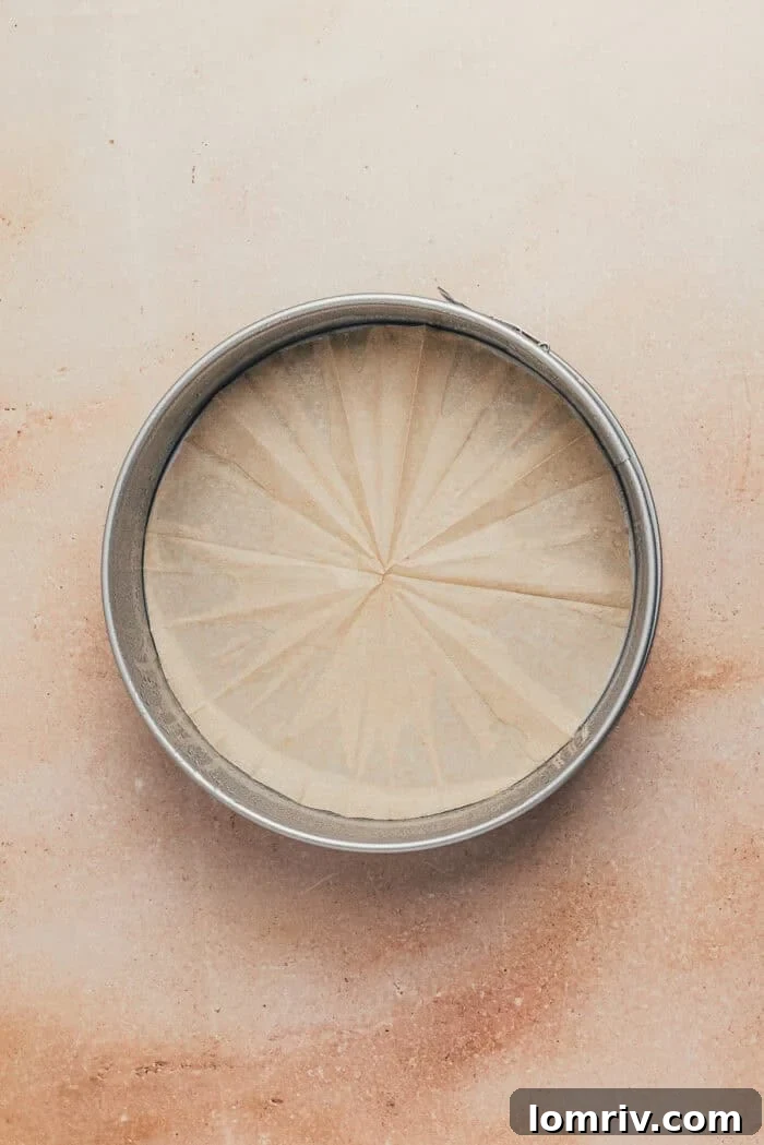 A pristine 9-inch round metal springform baking pan, meticulously prepared with cooking spray and lined with a circular piece of parchment paper at the bottom.