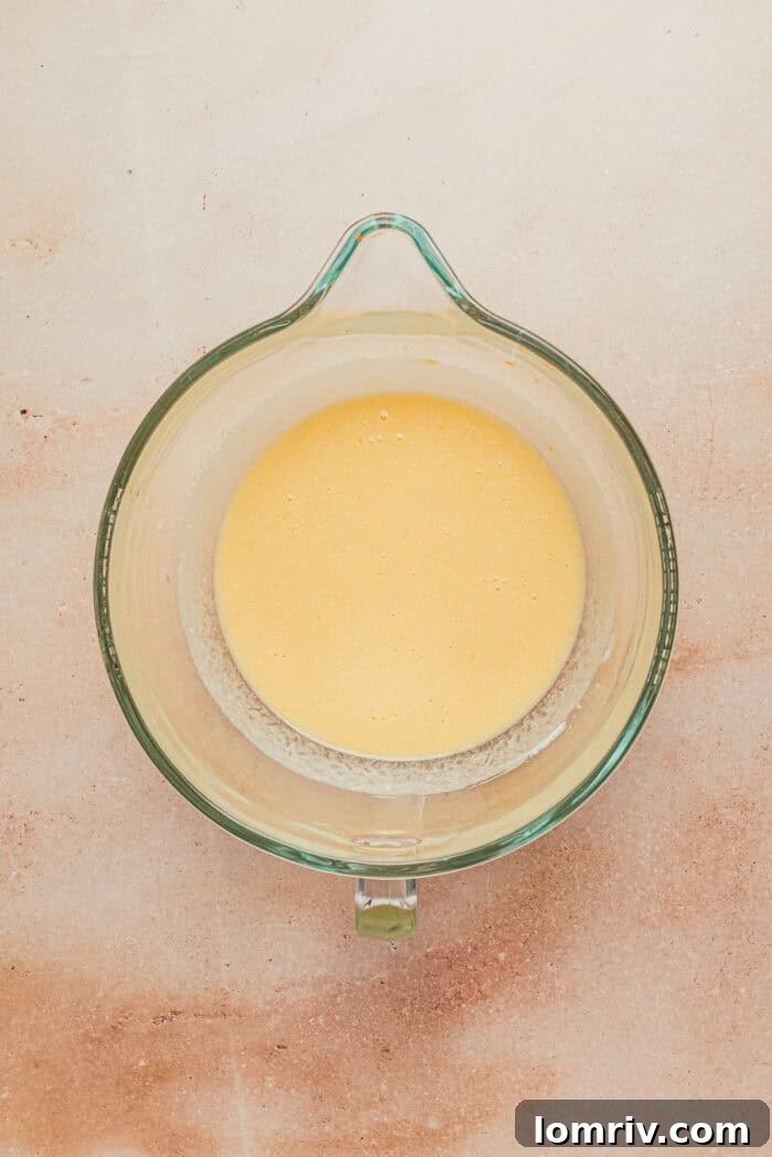 Large eggs, creamy whole milk ricotta cheese, granulated sugar, and vanilla extract are thoroughly mixed together in a stand mixer bowl, creating a smooth wet base.