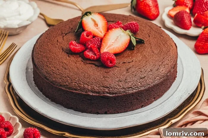 The exquisite chocolate ricotta cake, showcased on a rustic wooden platter with a colorful scattering of fresh berries and mint leaves, ready for a dessert table.