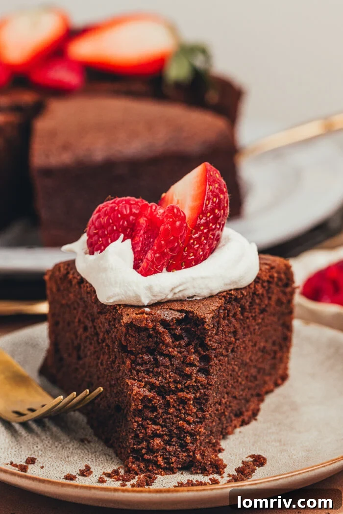 A mouth-watering slice of chocolate ricotta cake, topped with a delicate swirl of whipped cream and glistening fresh berries, ready to be savored.