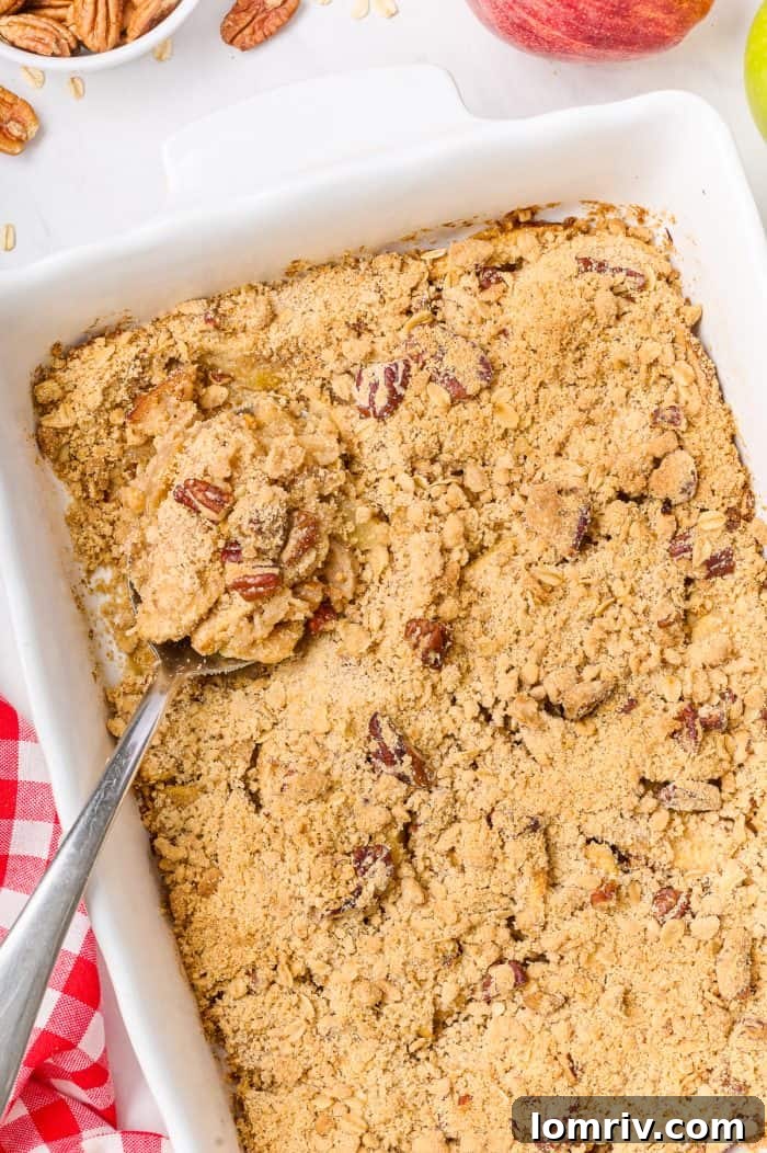 A freshly baked apple cardamom crisp, golden brown and bubbling, with a serving spoon taking a portion.