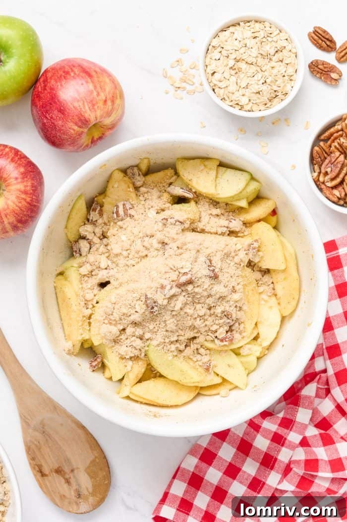 Sliced apples being lightly tossed with a portion of the streusel topping mixture in a white bowl.