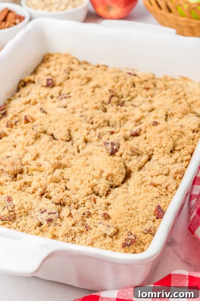 A top-down view of a freshly baked apple crisp with cardamom, showcasing its golden-brown, crumbly topping in a white ceramic baking dish.