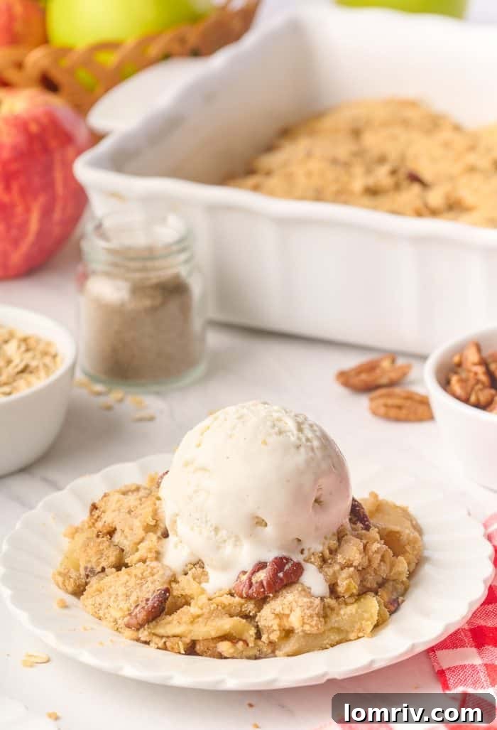 A beautifully plated serving of apple cardamom crisp, topped with melting vanilla ice cream, with the full baking dish visible in the soft-focus background.