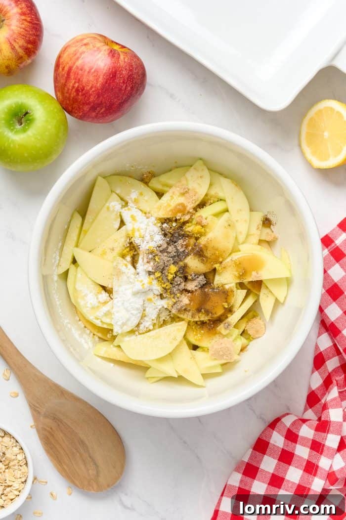 Sliced apples being tossed with brown sugar, cardamom, ginger, and lemon zest in a white mixing bowl.