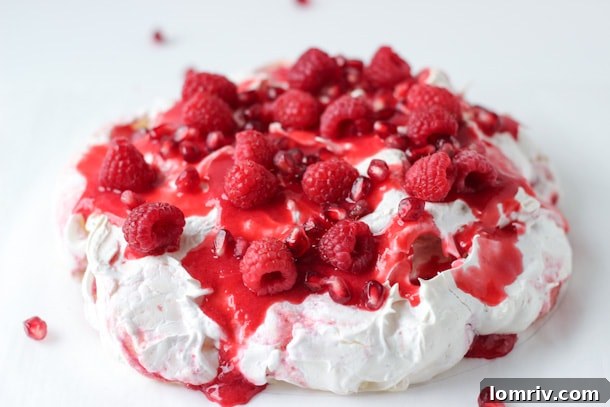 Close-up of fresh raspberries and pomegranate seeds adorning a slice of Pavlova, highlighting the juicy fruit.