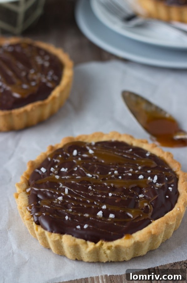 Close-up of a mini Caramelized Dark Chocolate Tart, garnished with whipped cream, caramel, and sea salt flakes.