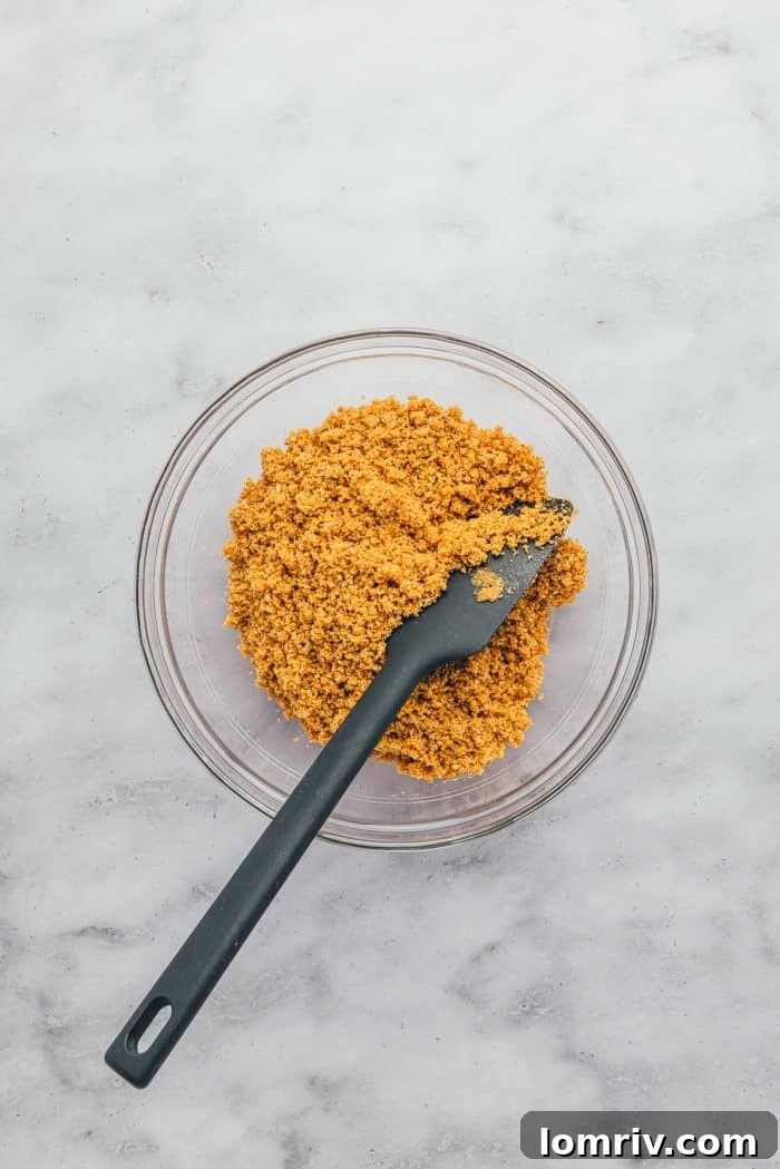 A glass bowl filled with graham cracker crumbs and butter, being mixed with a spatula for the pie crust.