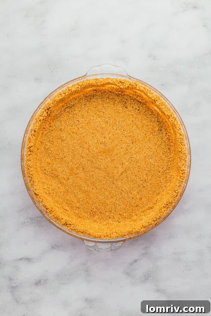 An unbaked graham cracker crust, perfectly pressed into a pie dish, ready for the oven.