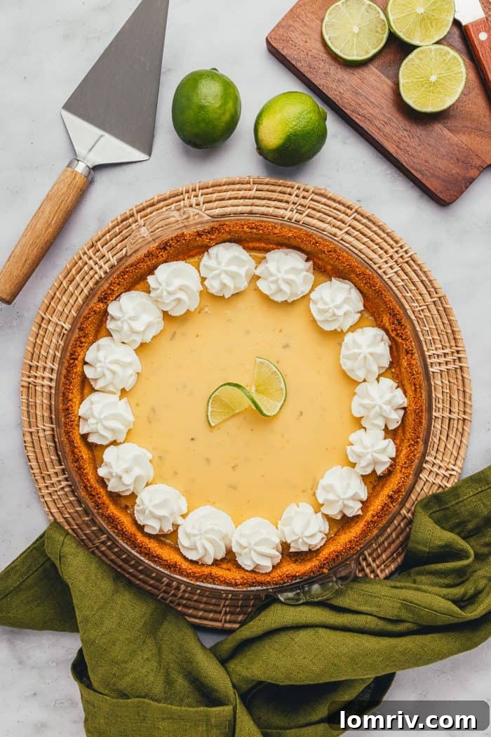 A whole Key Lime Pie, beautifully garnished with fresh Key Limes slices, set against a blurred background.