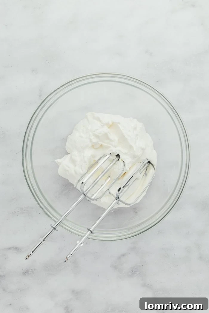 A glass bowl filled with freshly made, fluffy whipped cream, ready to adorn the Key Lime Pie.