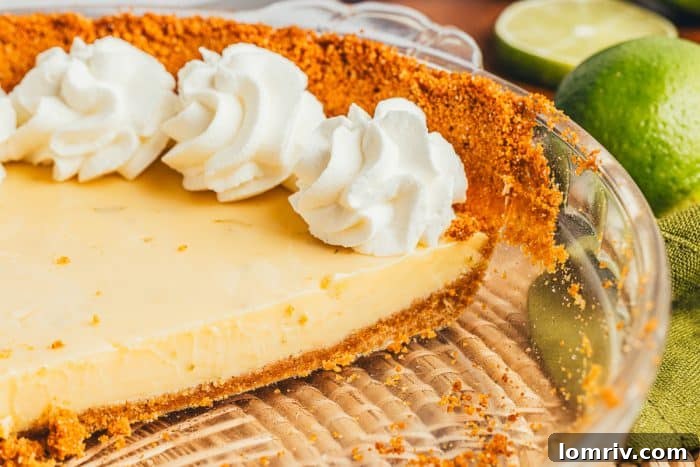 A whole Key Lime Pie resting in a clear glass pie dish, ready to be sliced and enjoyed.
