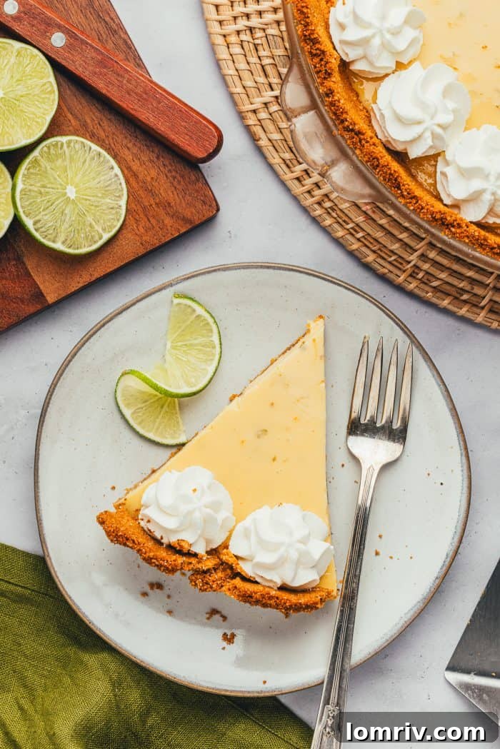 A perfectly portioned slice of Key Lime Pie on a white plate, accompanied by a fork, ready for tasting.