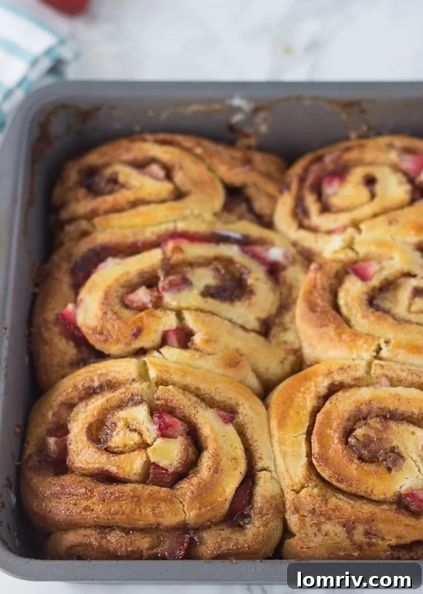 A tray of warm Strawberry Cinnamon Rolls, glistening with cream cheese frosting, ready to be enjoyed.