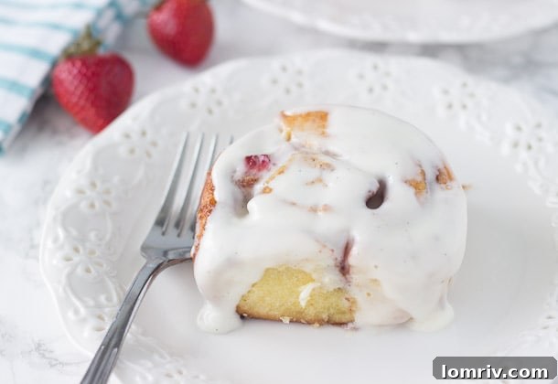 A close-up of a single Strawberry Cinnamon Roll, showing the delicate swirl and inviting frosting.