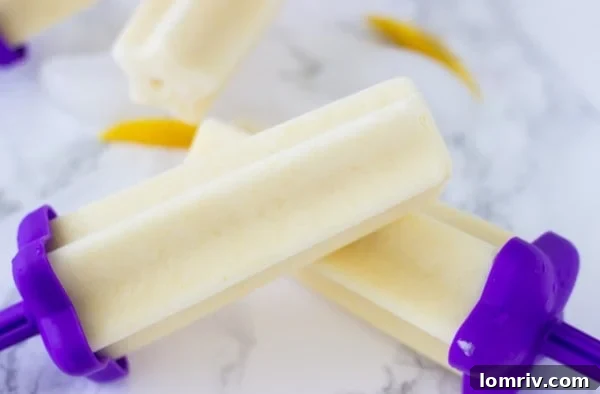 Close-up of vibrant yellow mango yogurt popsicles on a white background, ready to enjoy.