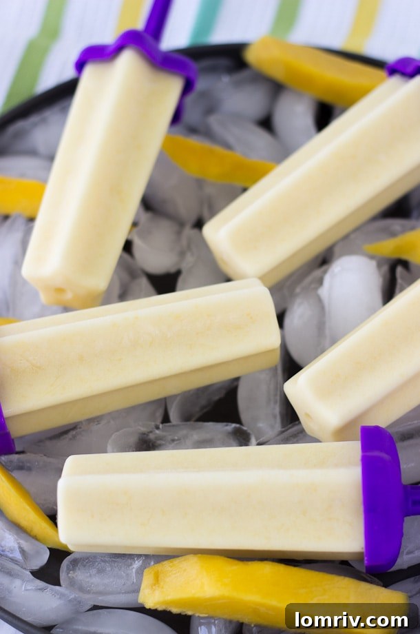 Three mango yogurt popsicles standing upright, showcasing their smooth texture and bright color.