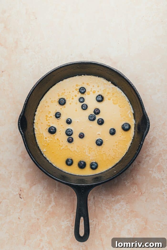 A hot skillet with Dutch baby pancake batter and blueberries.
