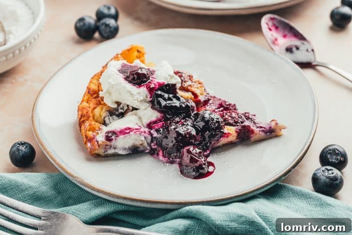A plate with a slice of blueberry lemon Dutch baby pancake with a dollop of whipped cream and blueberry compote.