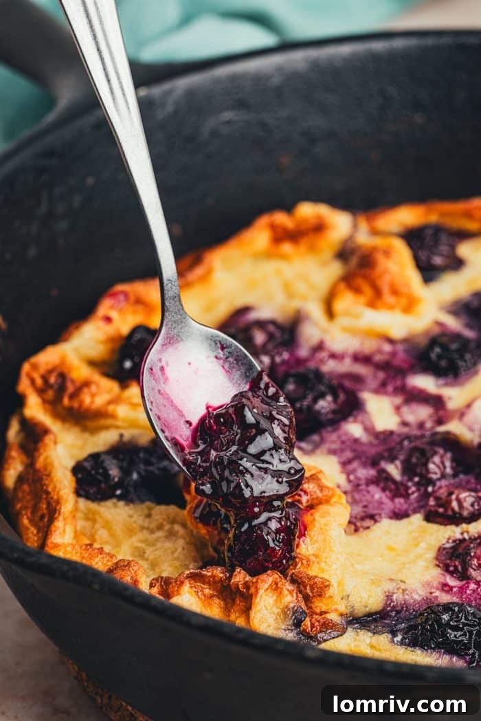 Adding homemade blueberry compote to a Dutch baby pancake.