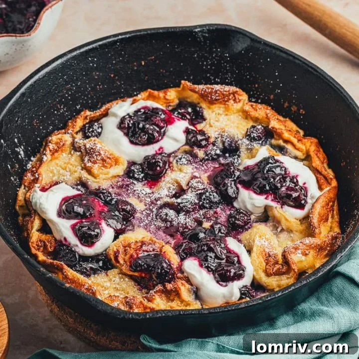 A skillet with a baked blueberry lemon Dutch baby pancake that is garnished with whipped cream and blueberry compote.
