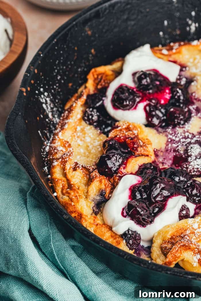 A closeup of a homemade blueberry Dutch baby pancake that is garnished with whipped cream and blueberries.