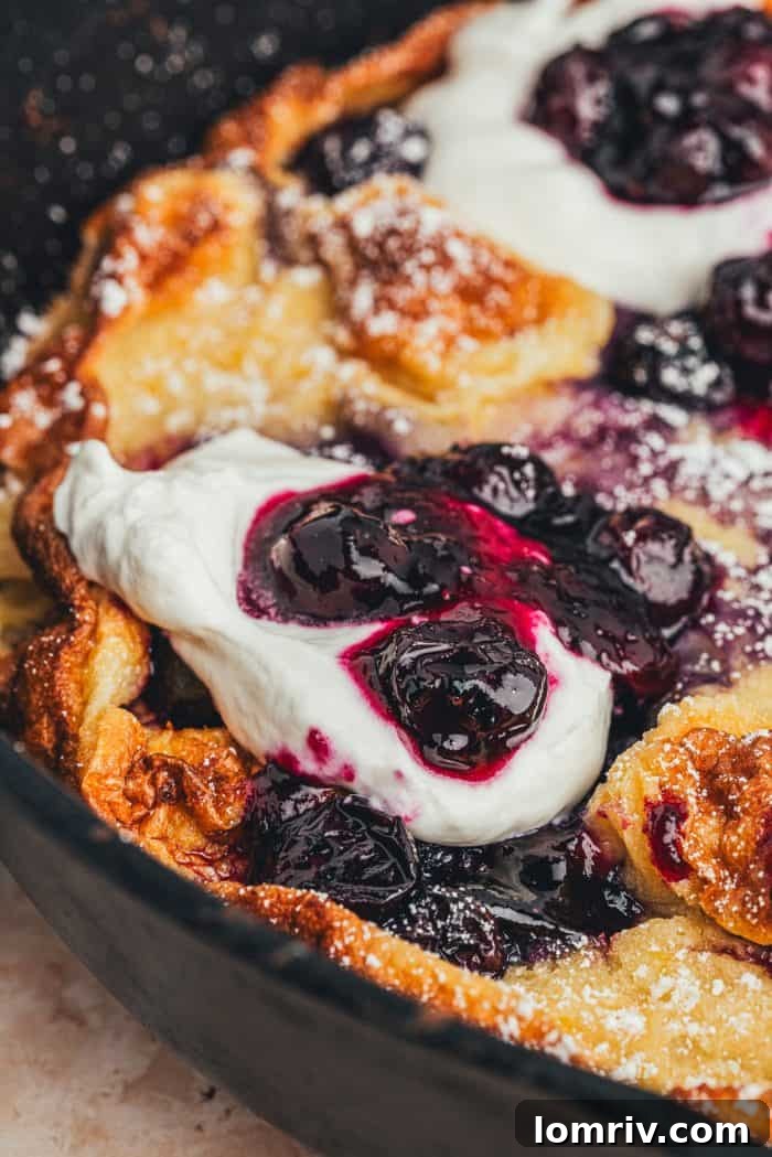 A closeup of a homemade blueberry Dutch baby pancake that is garnished with whipped cream and blueberries.