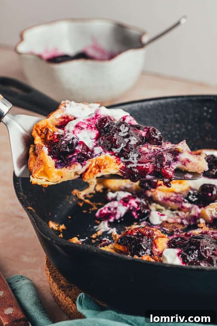 A closeup of a homemade blueberry Dutch baby pancake that is garnished with whipped cream and blueberries.