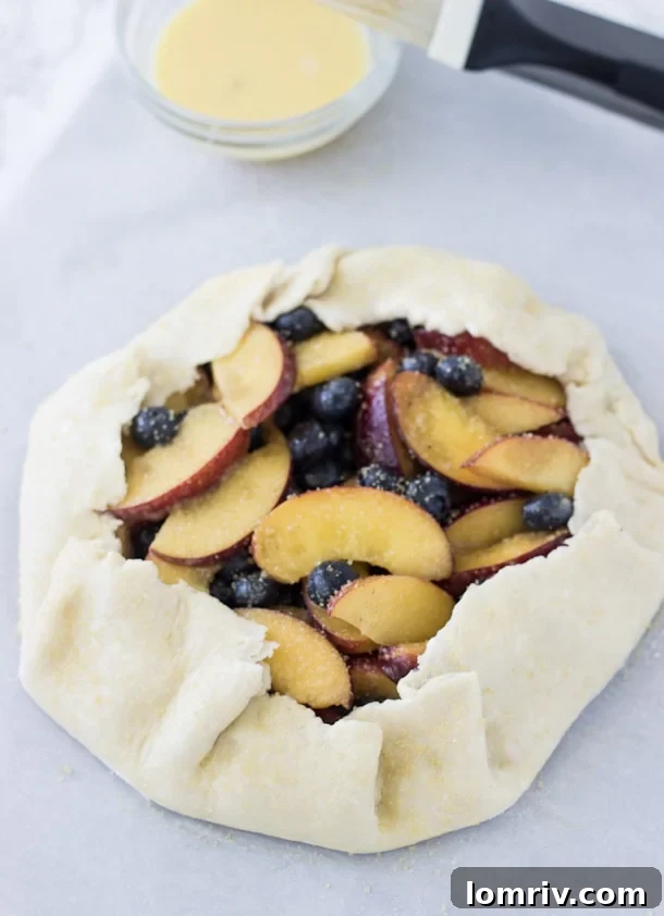 A close-up view of the golden, pleated crust of a peach blueberry galette, revealing the rich, purple-hued fruit filling within.