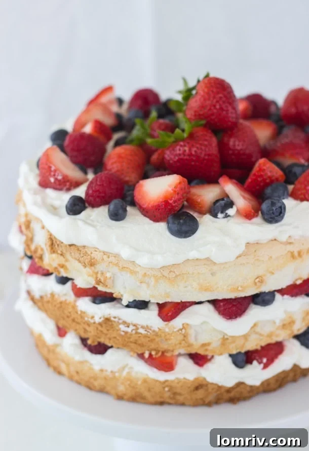 Layered Angel Food Cake with rich coconut whipped cream and a colorful topping of fresh strawberries, blueberries, and raspberries.