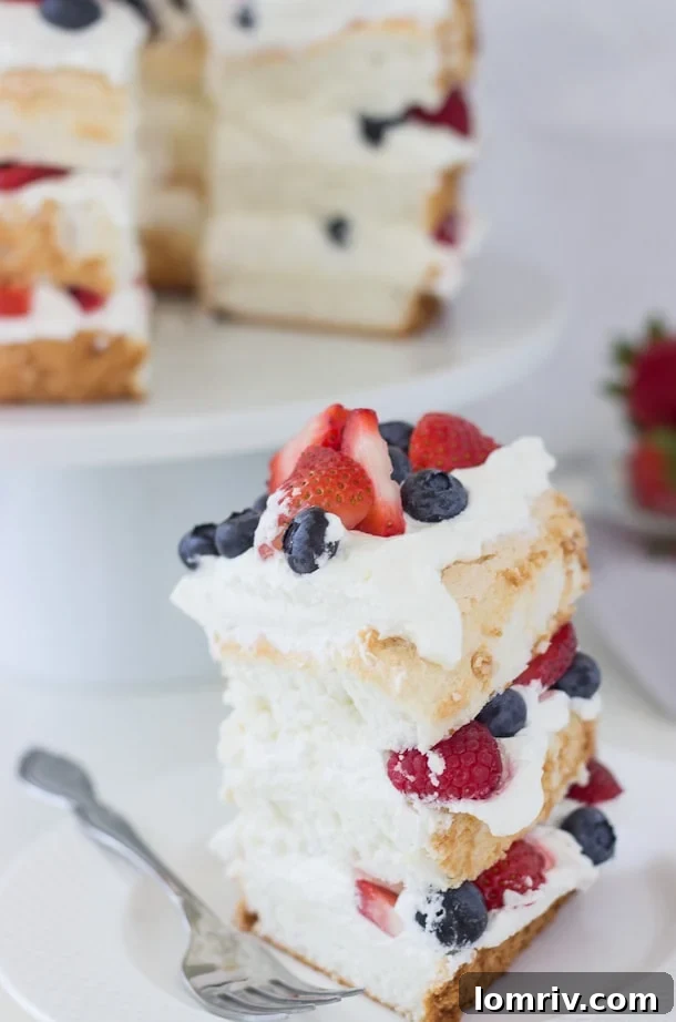 A stunning close-up of a patriotic Angel Food Cake, layered with coconut whipped cream and adorned with red, white, and blue berries.