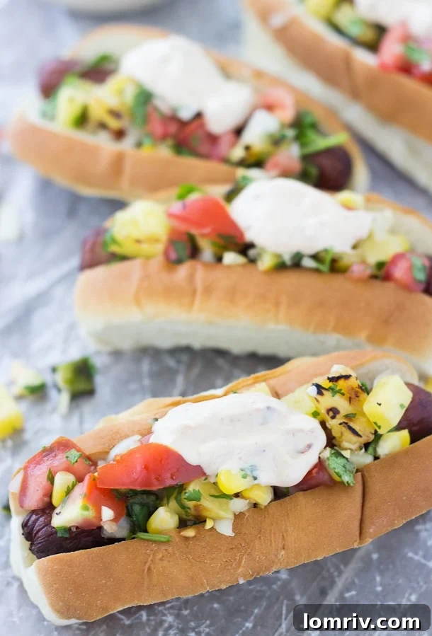 Beautifully dressed hot dogs featuring vibrant grilled corn and pineapple relish and creamy chipotle mayo