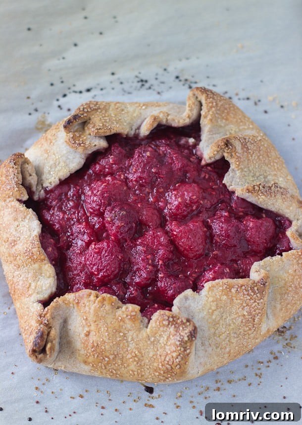 A beautifully rustic Raspberry Vanilla Bean Galette, brimming with juicy raspberries and rich vanilla bean flavors, on a wooden surface.