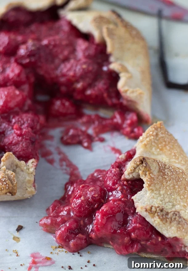 A full Raspberry Vanilla Bean Galette, freshly baked with a golden crust and glistening raspberry filling, on a cooling rack.