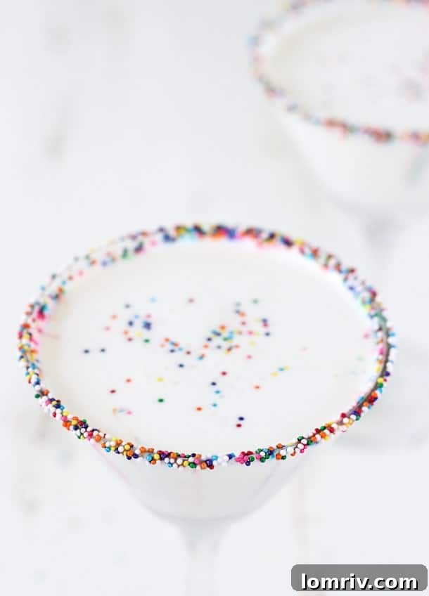 A vibrant Birthday Cake Martini with colorful sprinkles, embodying the festive spirit of a birthday celebration. The drink is sweet, chocolatey, and features a rim coated in honey and sprinkles, set against a blurred celebratory background.
