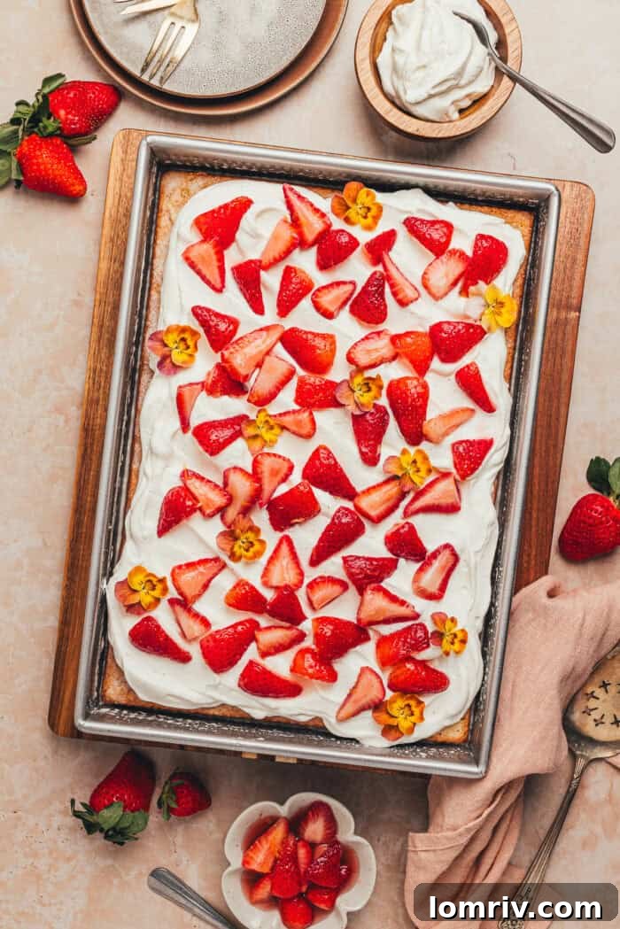A rectangular cake pan with a tres leches cake with strawberries, garnished with fresh berries and flowers.