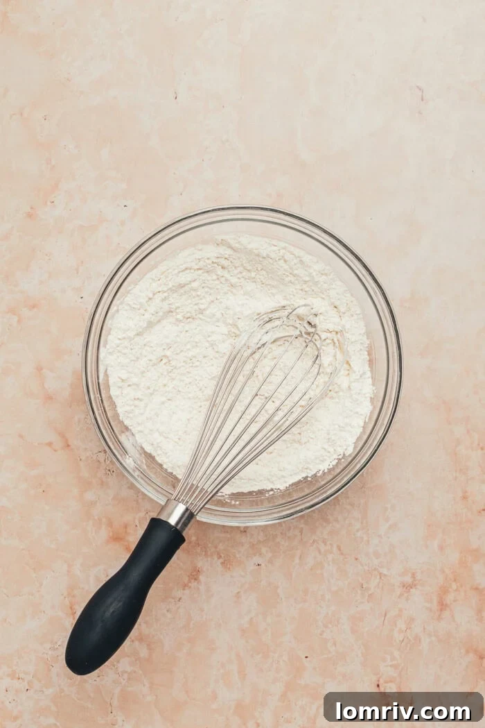 A clear glass bowl holding the sifted dry ingredients for the tres leches cake batter.