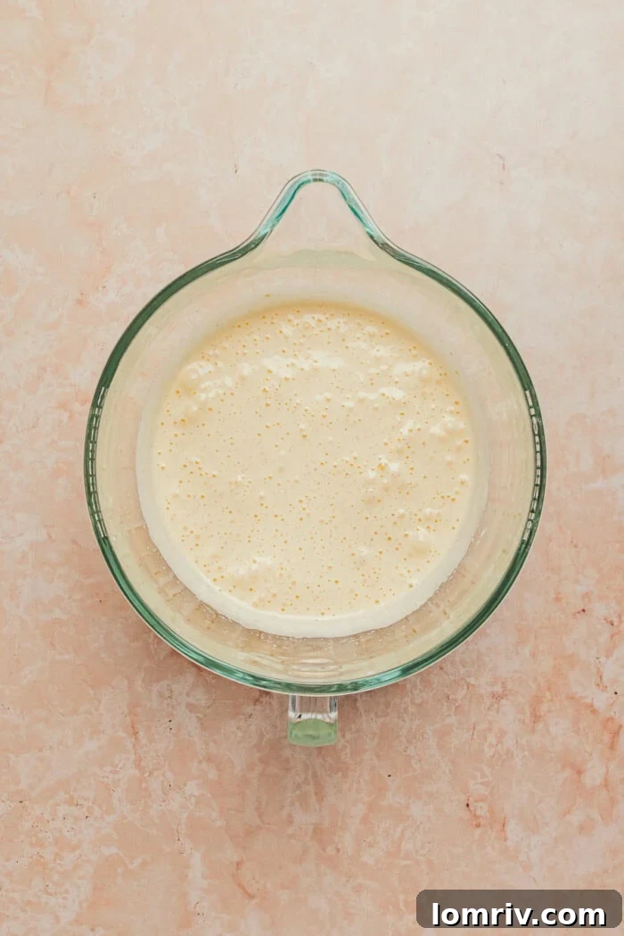 A stand mixer bowl containing the light yellow, voluminous batter for the tres leches cake.