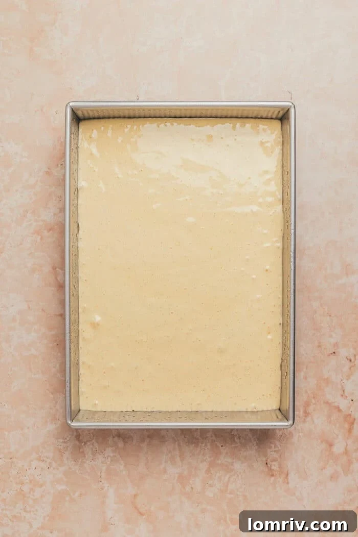 The cake batter evenly spread into a rectangular greased baking dish, ready for the oven.