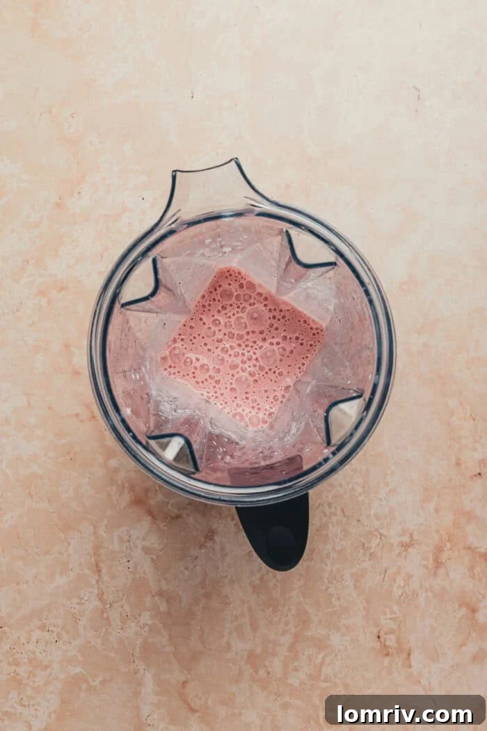 A blender filled with fresh strawberries and whole milk, ready to be blended for the strawberry milk mixture.
