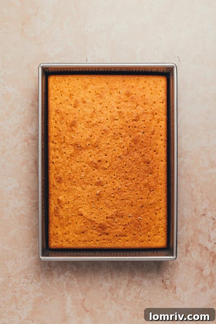 The baked tres leches cake with a pattern of small holes poked across its surface, ready for the milk soak.