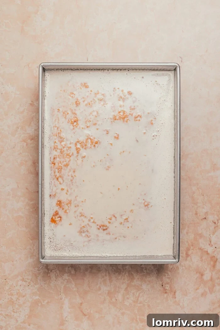 The homemade strawberry milk mixture being poured generously over the hole-poked tres leches cake.