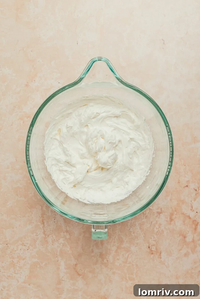 A glass mixing bowl filled with freshly whipped cream, showing its soft peaks.