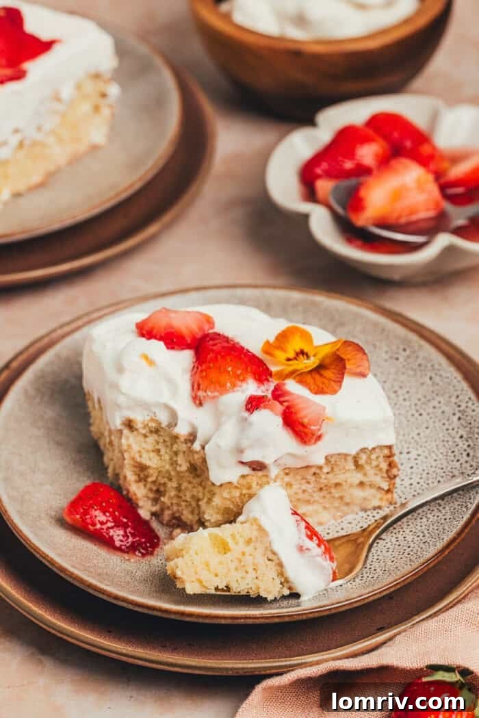 A close-up shot of a fork taking a bite from a slice of strawberry tres leches cake, showing the moist layers and topping.