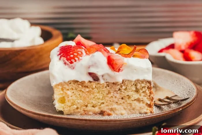 A vibrant slice of strawberry tres leches cake on a white plate, with a fork resting beside it, highlighting its delectable appearance.