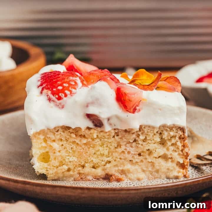 A slice of strawberry tres leches cake on a plate with a fork beside it.