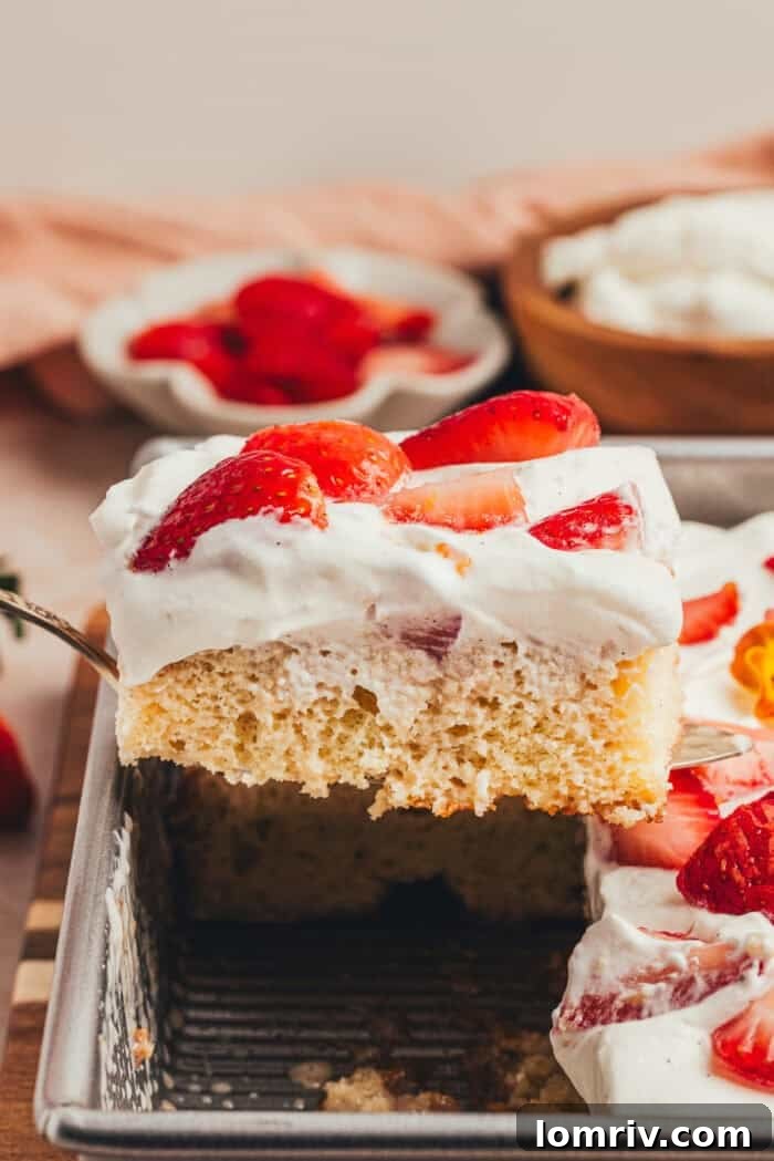 A serving of strawberry tres leches cake being lifted from the pan, showcasing its layers.